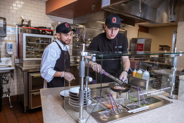 A chef instructor trains student employee how to cook vegetable with saute pan.