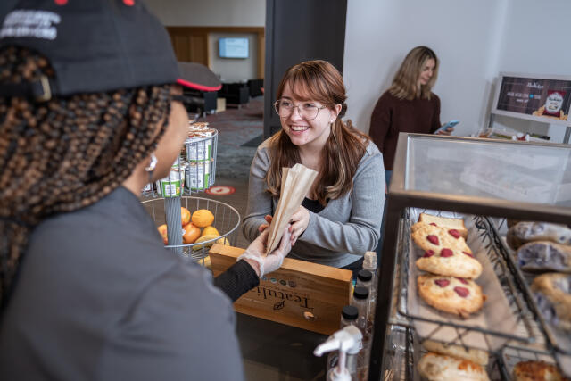 Student hands off a bakery item to a smiling student customer.