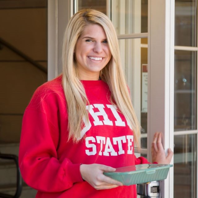 Ohio State student holding a green reusable container
